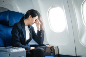 A woman in a formal suit sits in a window seat of an economy cla