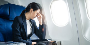 A woman in a formal suit sits in a window seat of an economy cla