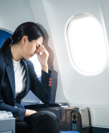A woman in a formal suit sits in a window seat of an economy cla
