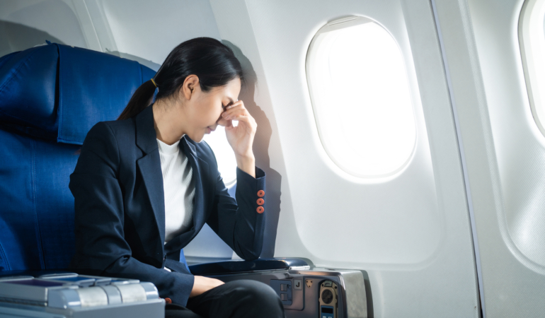 A woman in a formal suit sits in a window seat of an economy cla